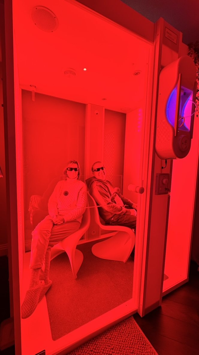 Two clients seated side by side in the red light booth, wearing eye protection
